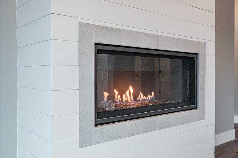 gas Fire place with white blocks and gray tile framing fireplace located on a gray wall with white bottom trim and dark wood floor with gray undertone