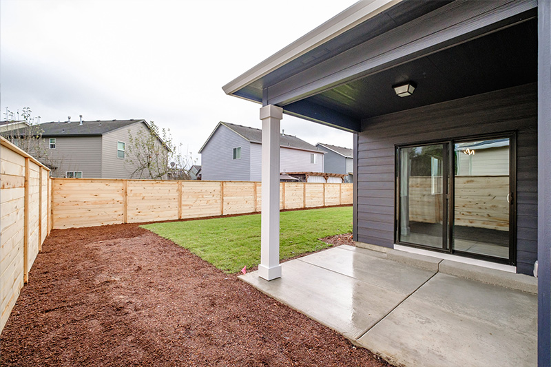 Picture of a newly built home with navy siding, a new wood fence, covered concrete patio and sliding glass doors in the backyard