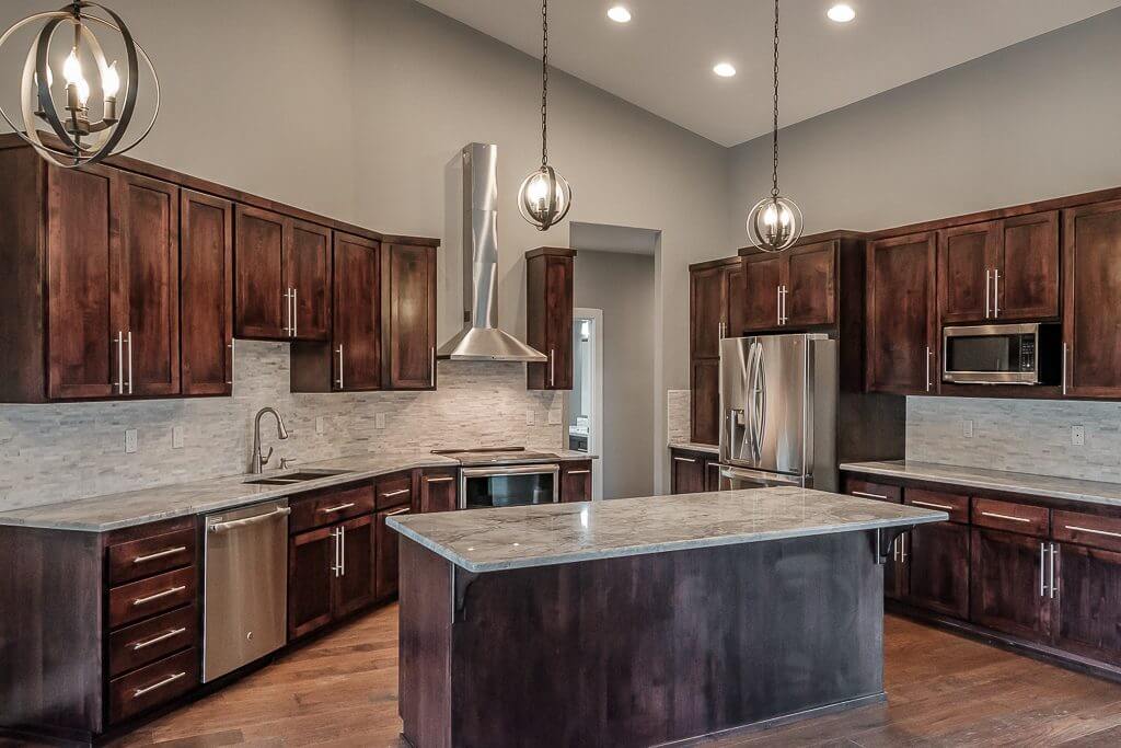 large kitchen with dark brown wood cabinets and island with gray rock countertops, stainless steel fixtures and appliances vaulted ceilings with canned lighting