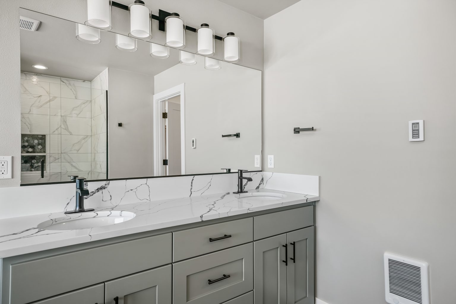 bathroom with greenish gray cabinets, and white marble counters with gray veining, dual sinks, large mirror and lighting fixtures