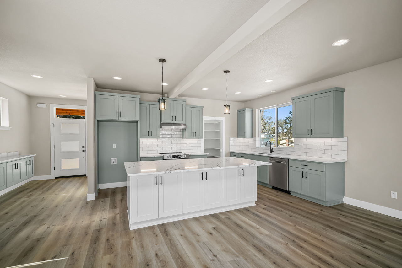 beautiful large, open kitchen with white tile backsplash, gray with green undertone cupboards, island, stainless steel appliances and natural lighting