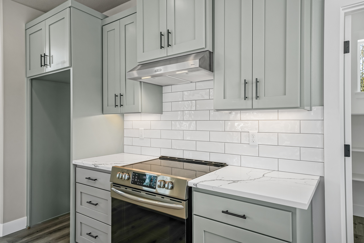 stove area of kitchen with stainless steel appliances, white brick looking tile backsplash, white with gray vein countertop and light cupboards
