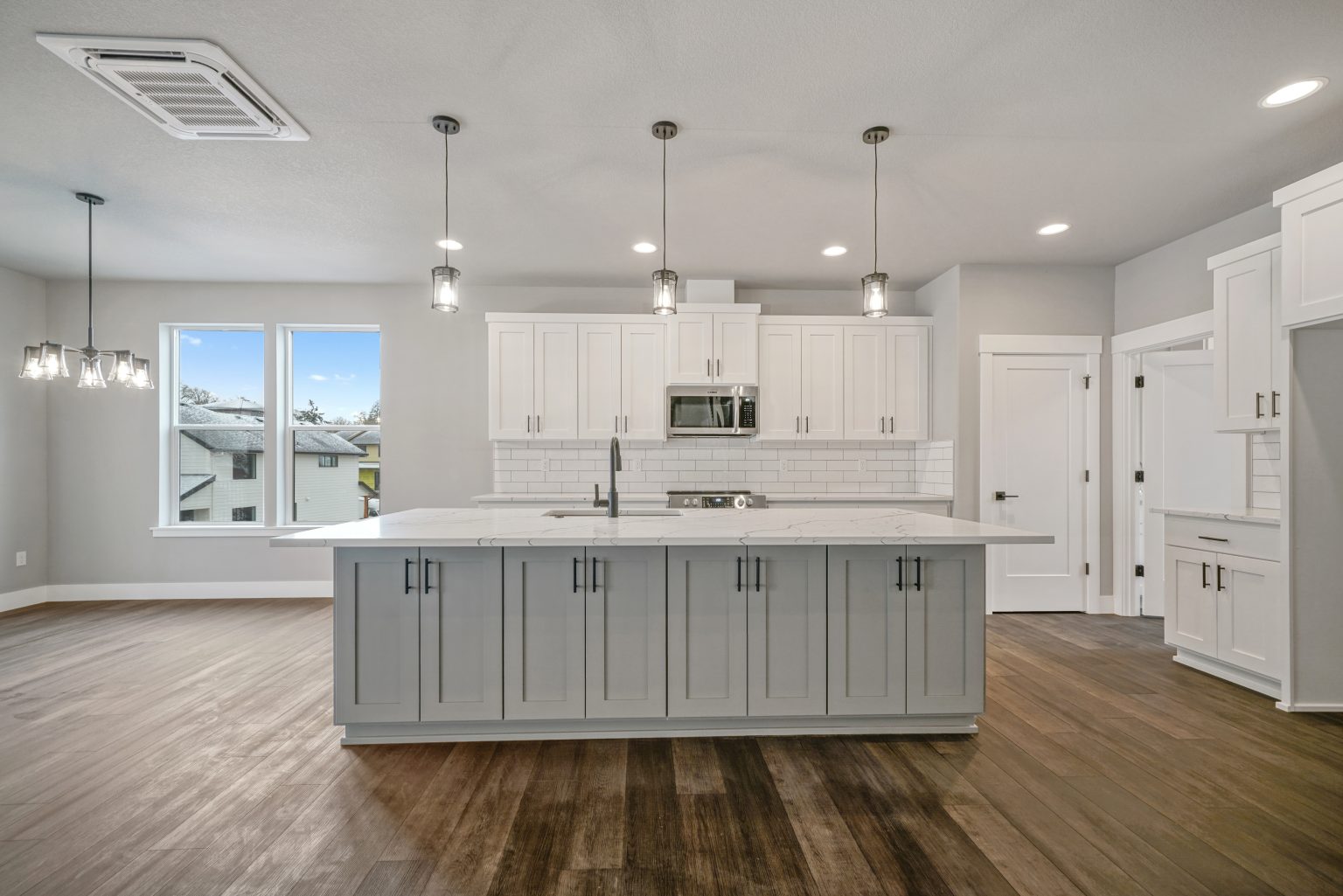 Spacious kitchen with island, white backsplash, white cupboards and doors, stainless steel appliances