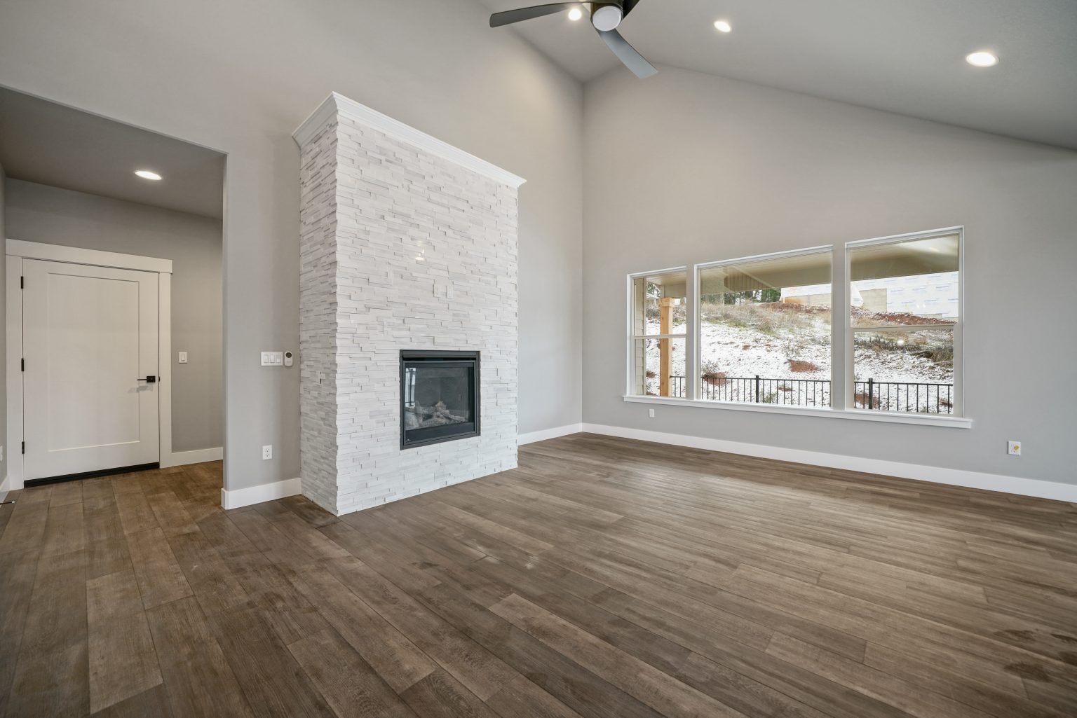 gorgeous living space with three large windows, high ceilings, white stone exposed wall with built-in gas fireplace and hardwood floors